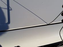 Fish your hook inside under the hood and through your window underneath and perhaps a flashlight get it hooked, then carefully drag it to the right until it pops.