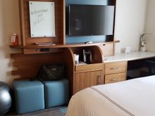 Desk with Keurig and refrigerator to the left. Electric sockets, with USB, below television. 