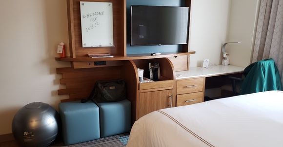 Desk with Keurig and refrigerator to the left. Electric sockets, with USB, below television. 