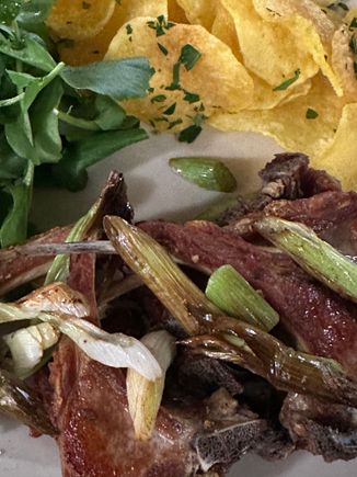 Astoundingly great little lamb chops, topped with roasted garlic scapes and accompanied by chips of potato and an arugula-type green