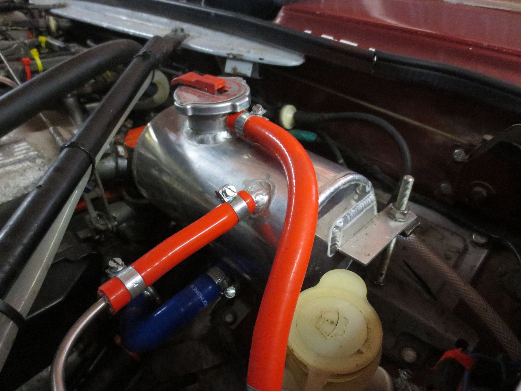 Custom header tank: blue hose goes to the heater return (this is the main connection to the systyem to fill it). Small hardline to red flexible is the bleed line from the radiator. Longer red flexible is to the atmospheric overflow