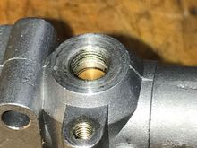 Original early style FA-65 carb with broken NVA removed. Note small, black window, next to brass at 2 O'Clock. This is the fuel entry port that accepts metered fuel from NVA. Also note threads stop just above that port. About 2mm below surface. This is as deep as you should thread the valve upon assembly.